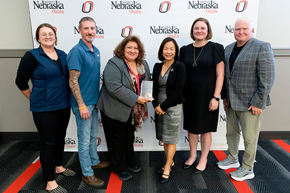 Six people pose for a group photo in front of a University of Nebraska Omaha step-and-repeat backdrop, with one person holding an award.